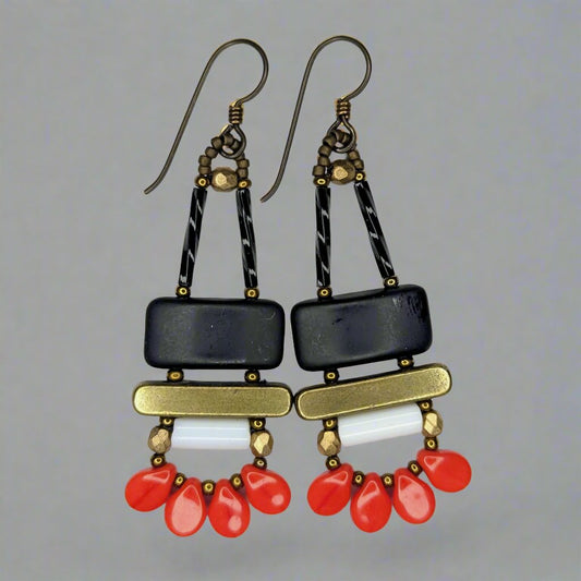 Long earrings that each have a wide matte black rectangle stacked on top of a brass colored bar. Under the bar there is a white tube and a swag of four warm red petal beads.