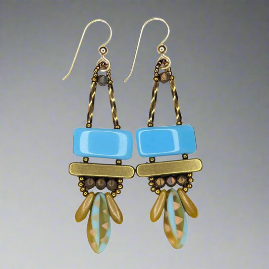 Long earrings that each have a wide light blue rectangle stacked on top of a brass colored bar. Under the bar there are small tan daggers on either side of a bigger blue and amber dagger with laser-etched copper accents.