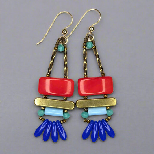 Long earrings that have a wide red rectangle stacked on top of a brass colored bar. Under the bar there is a light blue tube and a swag of four small blue dagger beads.